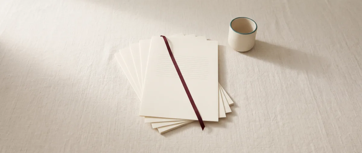Cinq feuilles crème en éventail avec un ruban oxblood et une tasse, sur une nappe en lin