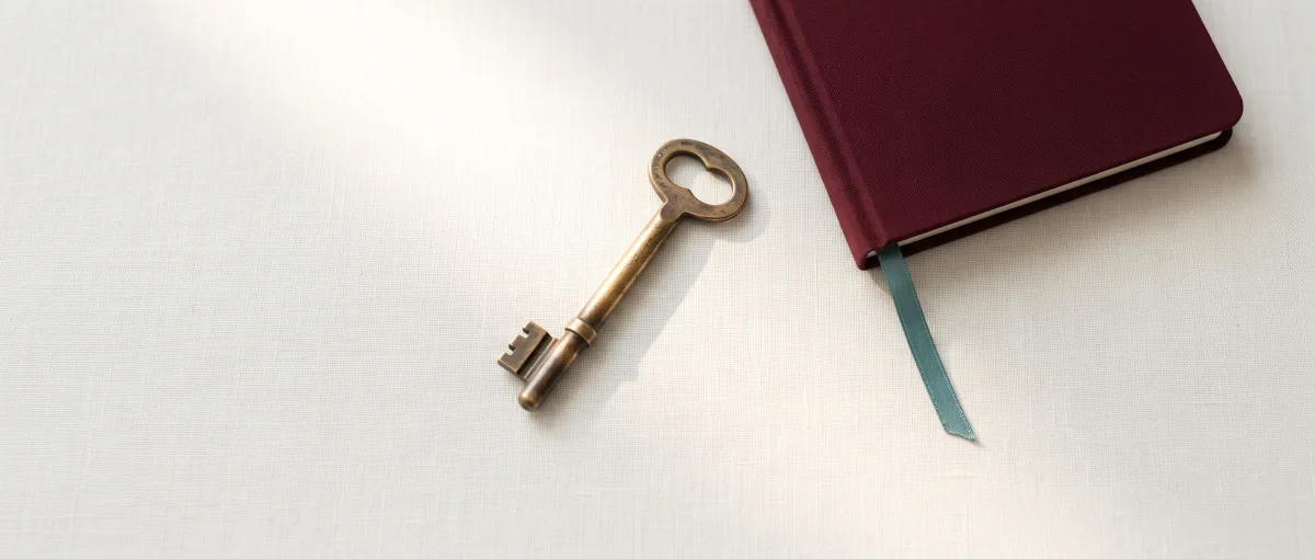 Une clé en laiton ancienne posée sur du lin crème, à côté d'un carnet oxblood au marque-page teal